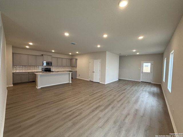 interior space featuring gray cabinets, electric range oven, decorative backsplash, a kitchen island with sink, and light hardwood / wood-style floors