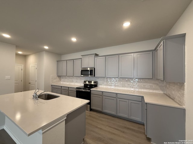 kitchen with gray cabinets, appliances with stainless steel finishes, sink, and a kitchen island with sink