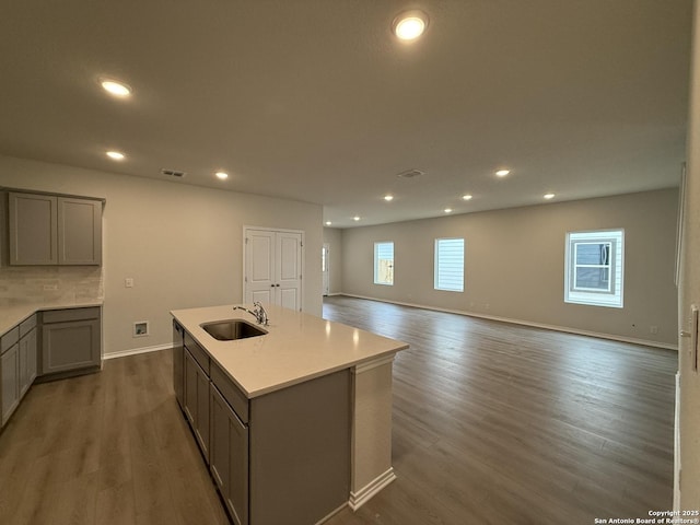 kitchen featuring sink, gray cabinets, tasteful backsplash, an island with sink, and dark hardwood / wood-style flooring