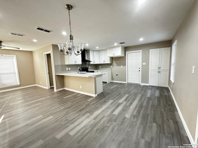 kitchen with pendant lighting, kitchen peninsula, electric range, white cabinetry, and wall chimney exhaust hood