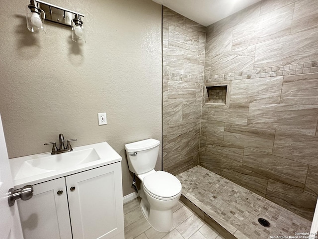 bathroom featuring toilet, tile patterned flooring, tiled shower, and vanity