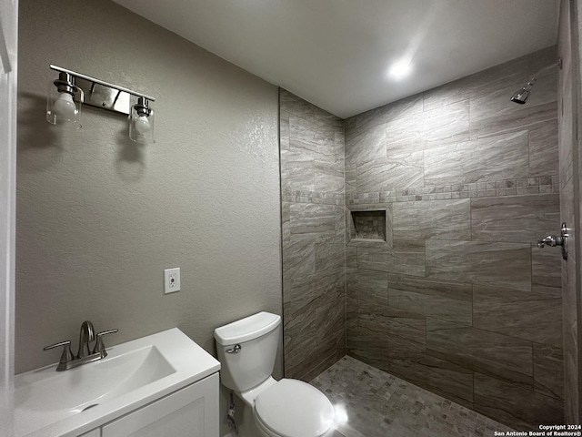 bathroom with toilet, tiled shower, and vanity