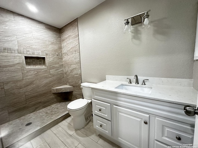 bathroom featuring toilet, vanity, and tiled shower