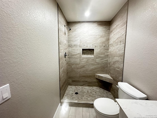 bathroom featuring toilet, a tile shower, and vanity