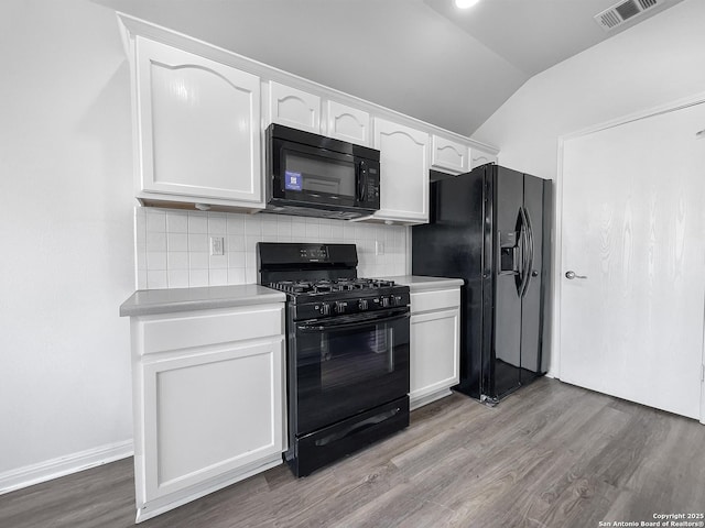 kitchen featuring black appliances, white cabinetry, decorative backsplash, vaulted ceiling, and hardwood / wood-style flooring