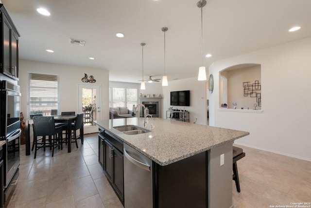 kitchen with a center island with sink, dishwasher, light stone countertops, pendant lighting, and sink