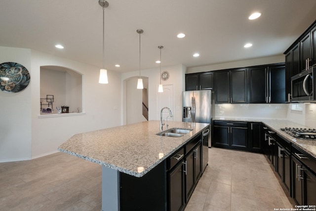 kitchen featuring a center island with sink, stainless steel appliances, decorative backsplash, decorative light fixtures, and sink