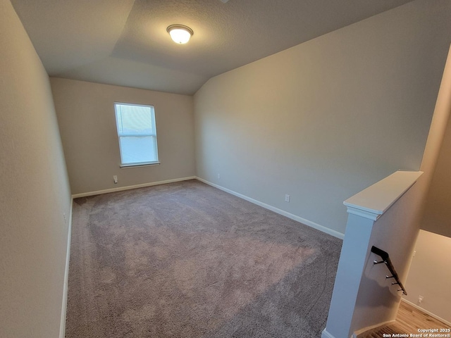 empty room with light colored carpet, a textured ceiling, and vaulted ceiling