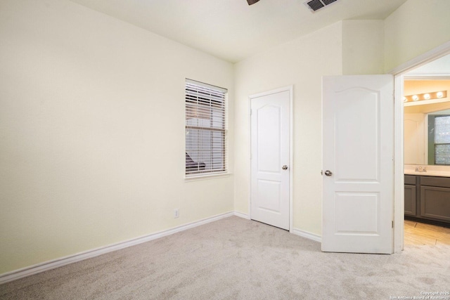 unfurnished bedroom featuring sink, ensuite bath, and light colored carpet