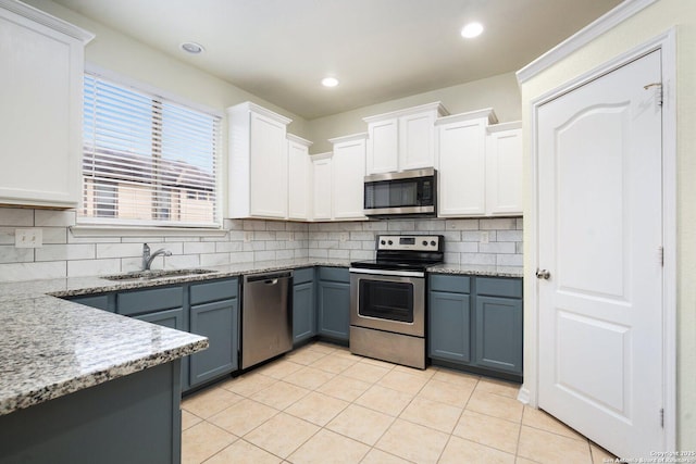 kitchen with sink, light tile patterned floors, appliances with stainless steel finishes, white cabinets, and backsplash