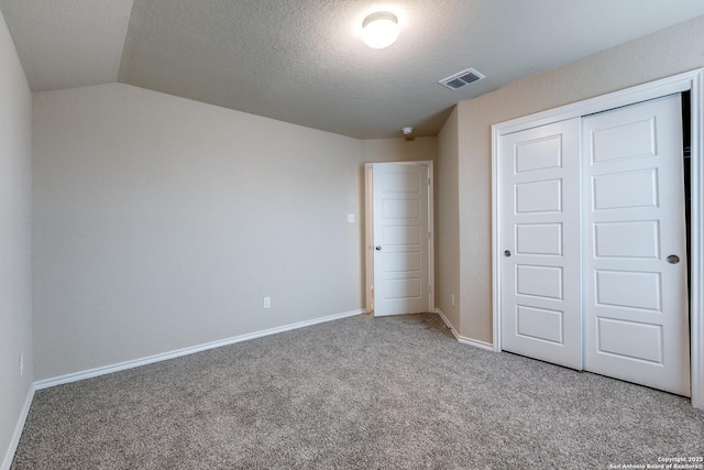 unfurnished bedroom featuring carpet, a closet, a textured ceiling, and vaulted ceiling