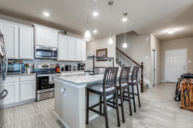 kitchen with appliances with stainless steel finishes, white cabinets, a center island with sink, and decorative light fixtures