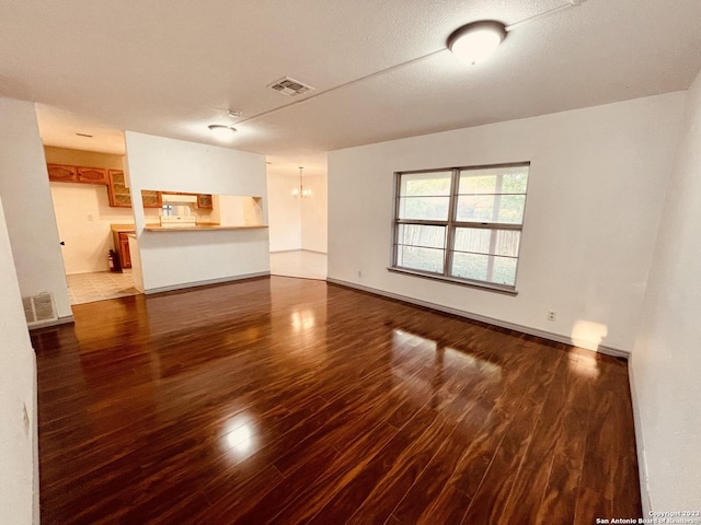 unfurnished living room featuring dark wood-type flooring, a textured ceiling, and a notable chandelier