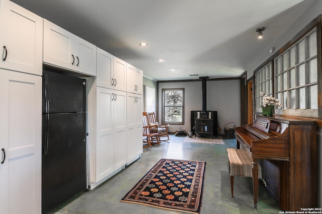 kitchen with black refrigerator, white cabinets, a wood stove, and concrete flooring