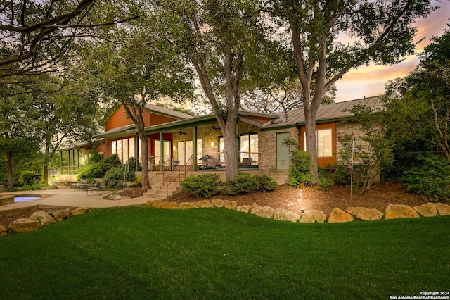 back house at dusk featuring a lawn and a patio area