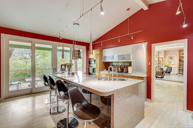 kitchen with a center island with sink, beam ceiling, pendant lighting, plenty of natural light, and high vaulted ceiling