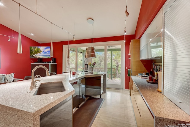 kitchen featuring a kitchen island with sink, track lighting, light stone countertops, pendant lighting, and sink