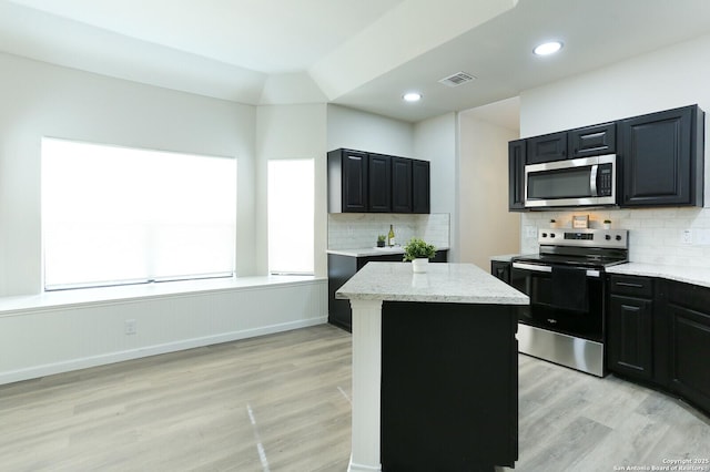 kitchen with a kitchen island, decorative backsplash, light wood-type flooring, appliances with stainless steel finishes, and light stone counters