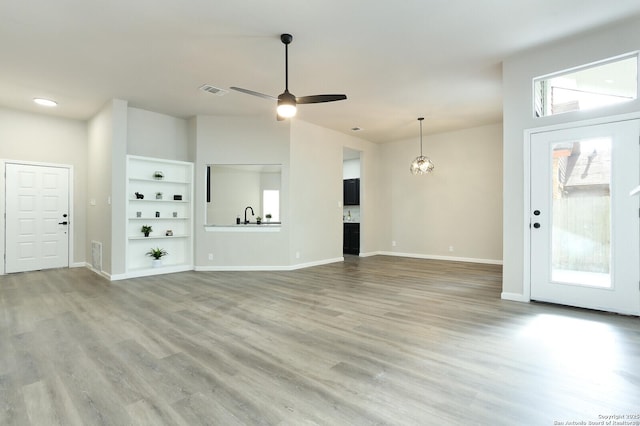 unfurnished living room with ceiling fan, built in shelves, sink, and light hardwood / wood-style floors