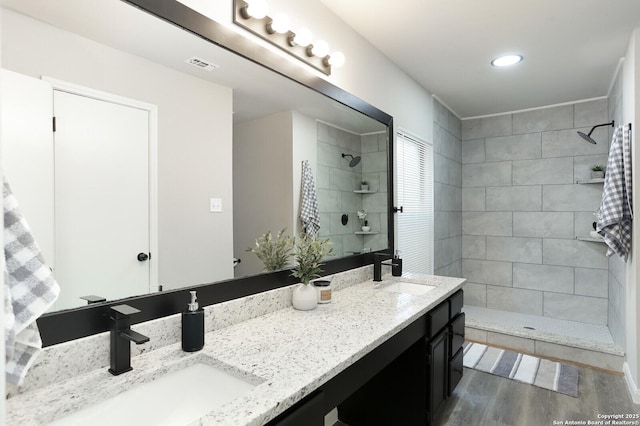 bathroom featuring hardwood / wood-style flooring, tiled shower, and vanity