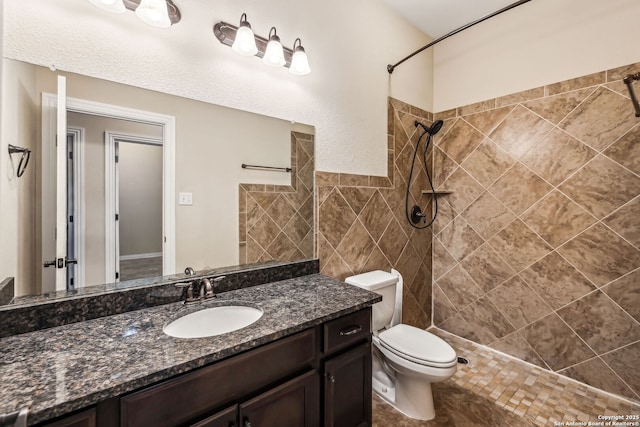 bathroom featuring tile walls, toilet, vanity, and a tile shower