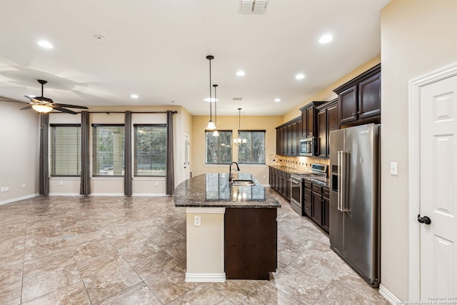 kitchen with decorative light fixtures, a center island with sink, dark stone counters, dark brown cabinets, and high quality appliances