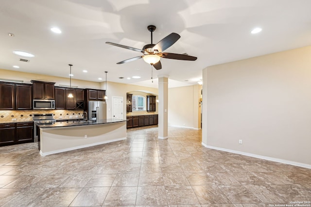 kitchen featuring tasteful backsplash, ceiling fan, a kitchen island, appliances with stainless steel finishes, and decorative columns