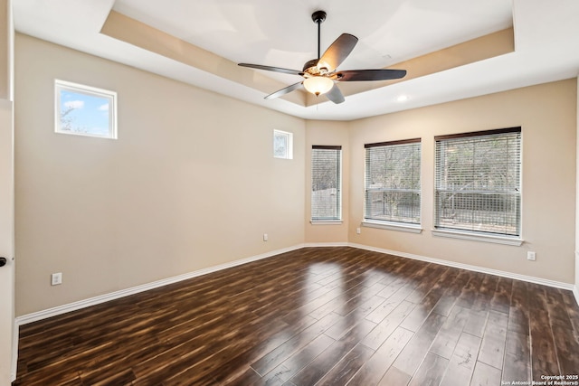 unfurnished room with a raised ceiling, ceiling fan, and dark hardwood / wood-style flooring