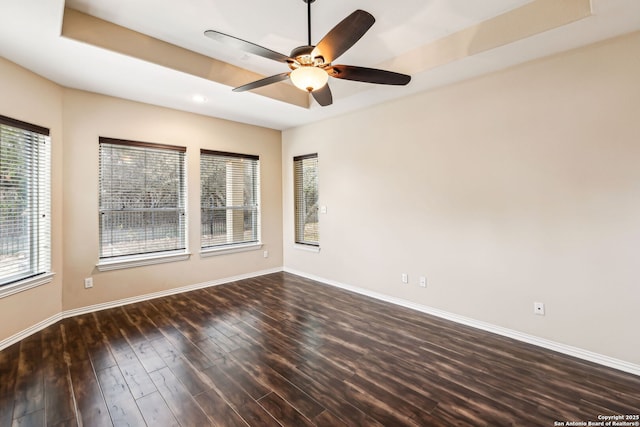 spare room with ceiling fan, dark hardwood / wood-style flooring, plenty of natural light, and a tray ceiling