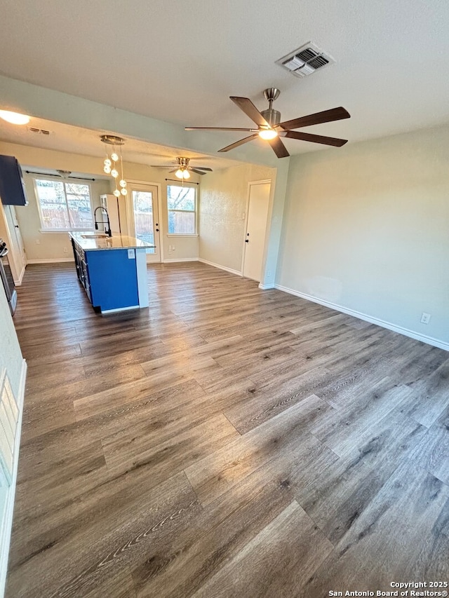 unfurnished living room featuring dark wood-type flooring, ceiling fan, a healthy amount of sunlight, and sink