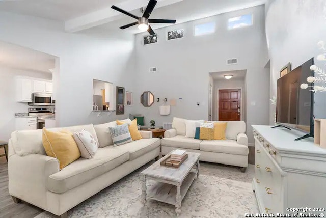 living room featuring beam ceiling, light wood-type flooring, a towering ceiling, and ceiling fan