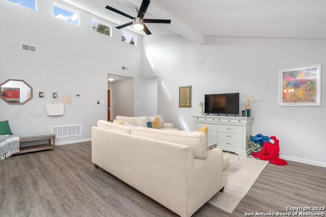 living room with ceiling fan, a high ceiling, beam ceiling, and light wood-type flooring