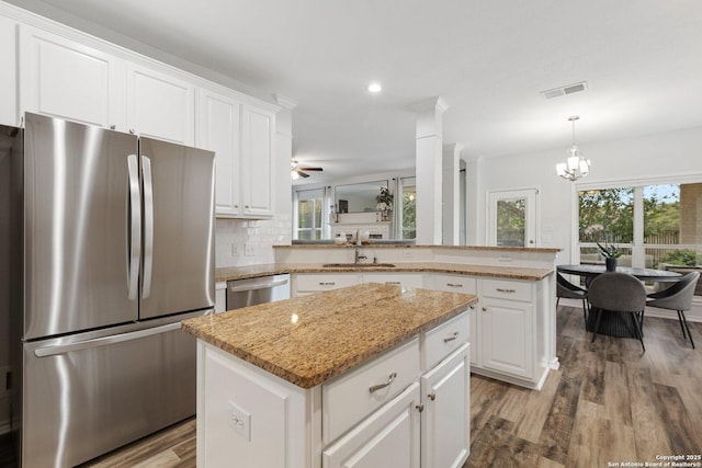 kitchen with a peninsula, a kitchen island, a sink, visible vents, and appliances with stainless steel finishes