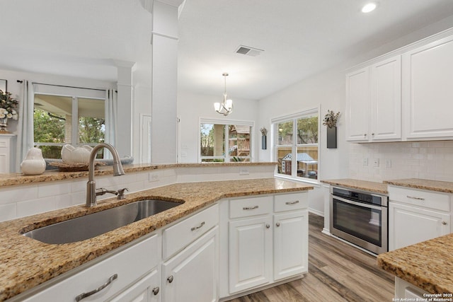 kitchen with oven, a sink, visible vents, decorative backsplash, and light wood finished floors