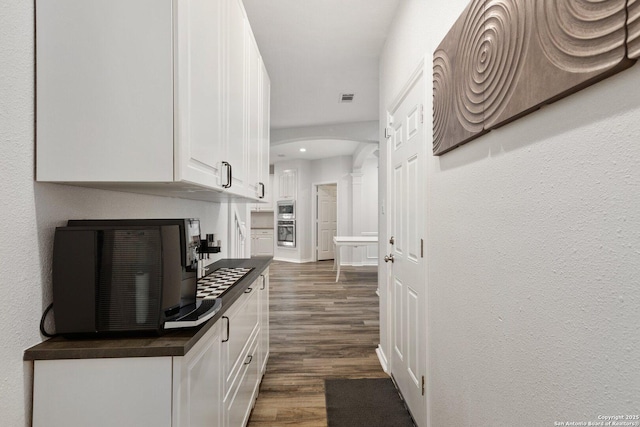 hall with arched walkways, a textured wall, dark wood-type flooring, visible vents, and baseboards