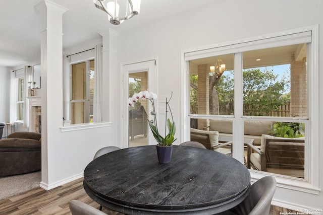 dining area with a fireplace, a notable chandelier, ornate columns, wood finished floors, and baseboards