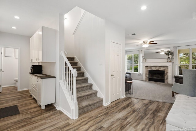 stairway with a wealth of natural light, a fireplace, recessed lighting, and wood finished floors