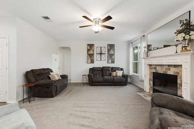 living area with arched walkways, ceiling fan, a fireplace with flush hearth, visible vents, and carpet