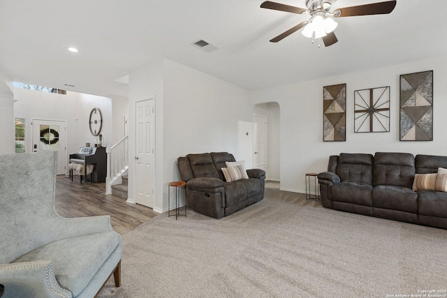 living room featuring arched walkways, visible vents, baseboards, a ceiling fan, and stairway