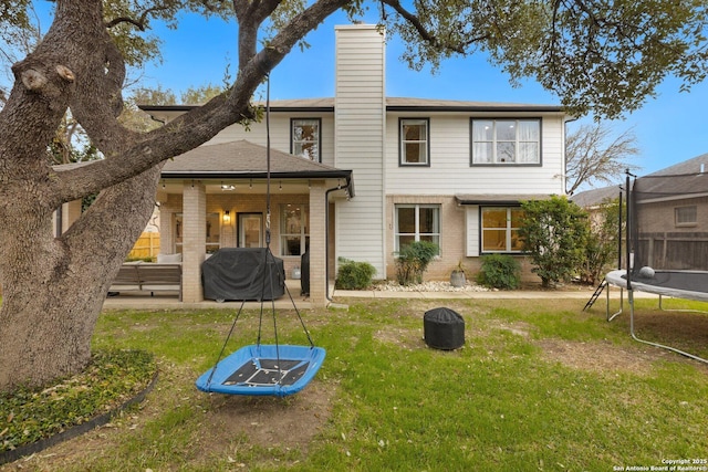 rear view of property featuring a trampoline, brick siding, a yard, a patio, and a chimney