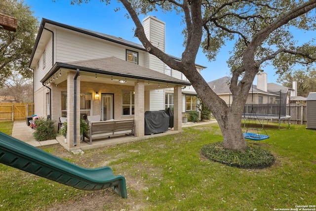 rear view of property featuring a trampoline, brick siding, a patio, a lawn, and a fenced backyard