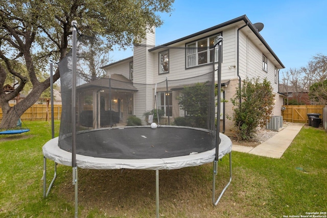 rear view of property with a trampoline, a chimney, fence, and a yard