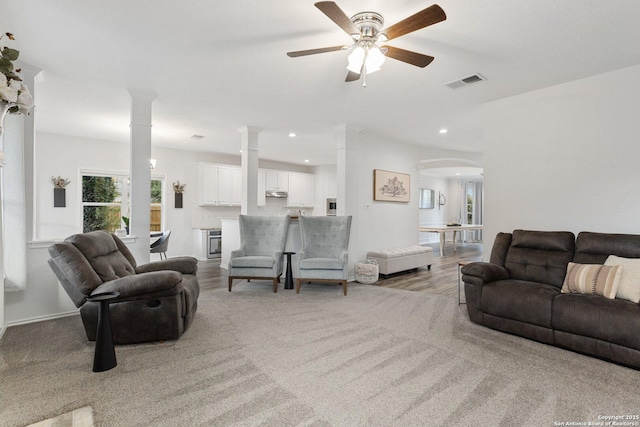 carpeted living area with arched walkways, recessed lighting, a ceiling fan, visible vents, and ornate columns