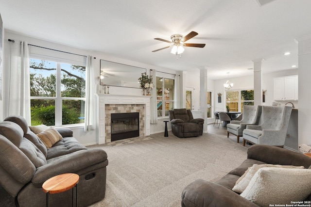 carpeted living room with ceiling fan with notable chandelier, baseboards, a tile fireplace, and ornate columns