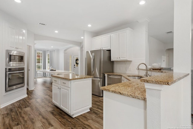 kitchen featuring arched walkways, stainless steel appliances, dark wood-style flooring, a sink, and a center island