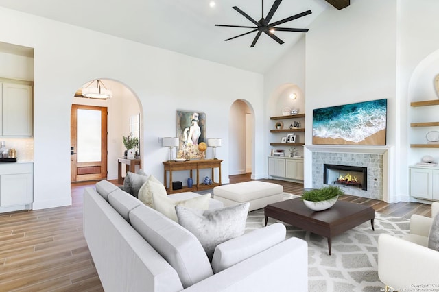 living room featuring ceiling fan, a fireplace, high vaulted ceiling, beam ceiling, and light hardwood / wood-style flooring