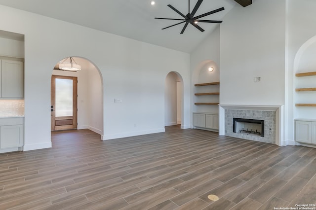 unfurnished living room featuring ceiling fan, light wood-type flooring, a tile fireplace, and high vaulted ceiling