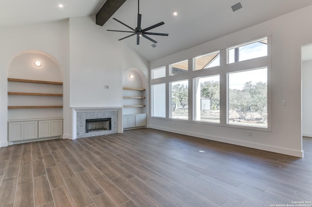 unfurnished living room with built in features, high vaulted ceiling, ceiling fan, a tile fireplace, and beam ceiling