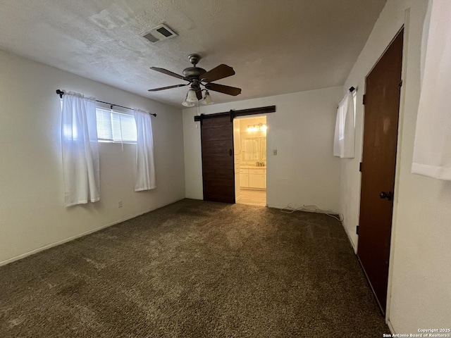 unfurnished bedroom featuring ceiling fan, a barn door, carpet, connected bathroom, and a textured ceiling