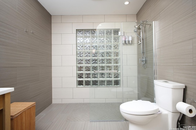 bathroom with toilet, vanity, tile walls, tile patterned floors, and a tile shower